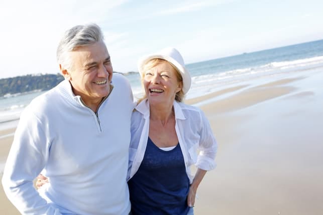 a mature couple smiling and having a walk on a beach together