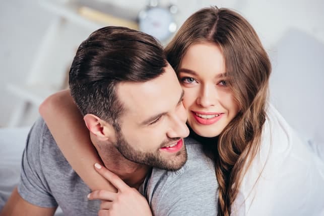 a young woman is hugging her boyfriend’s neck