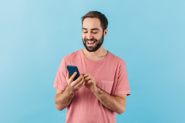 a happy man in a pink shirt is using his smartphone