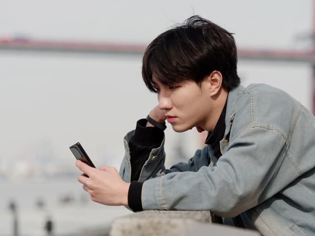a young Asian man using his smartphone while being visibly unhappy