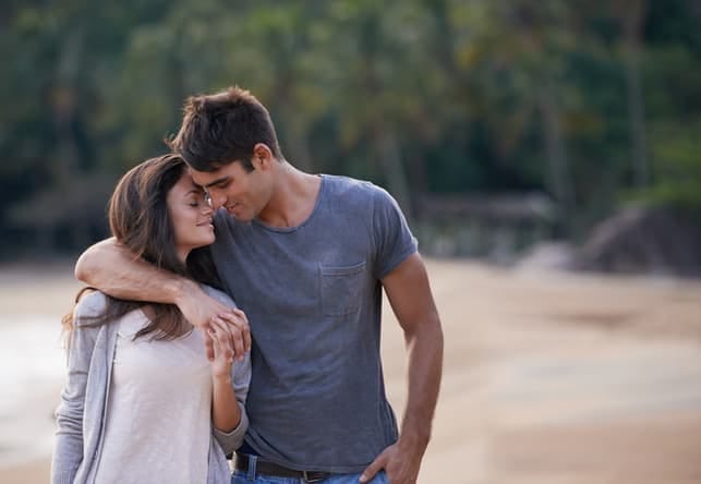 a young couple is walking on the beach