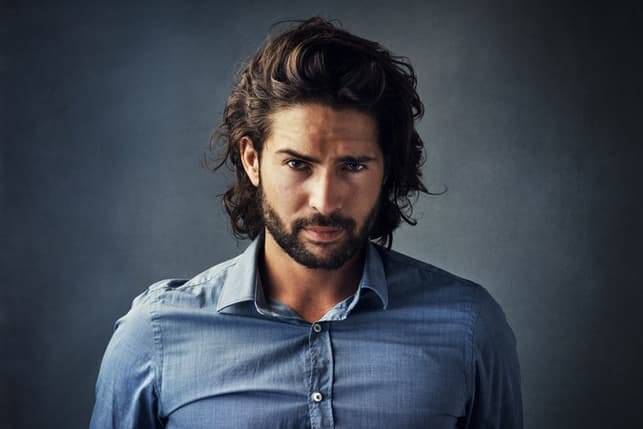 a handsome bearded man with thick curly hair is posing in a blue shirt