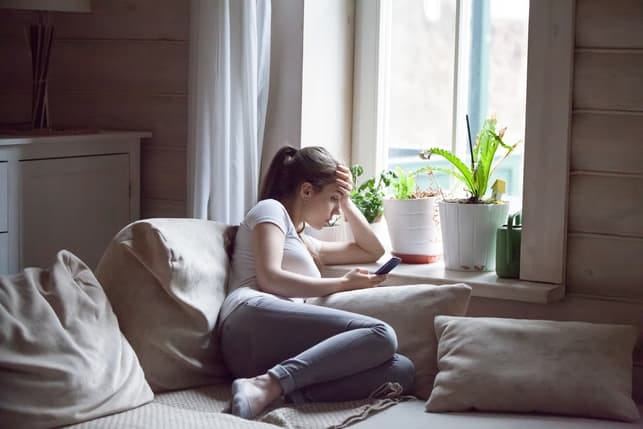 a sad woman checking her phone while lying on her bed