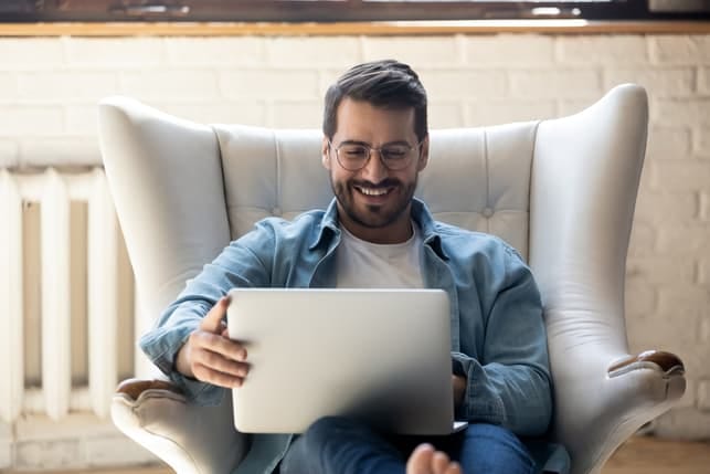 a happy bearded man is using his laptop at home
