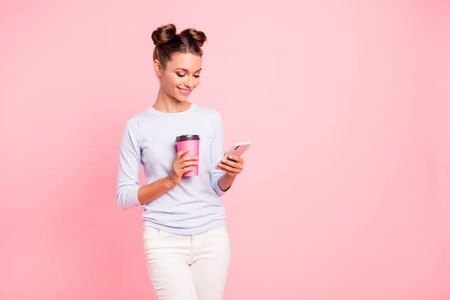 a woman is checking her phone while holding a coffee cup