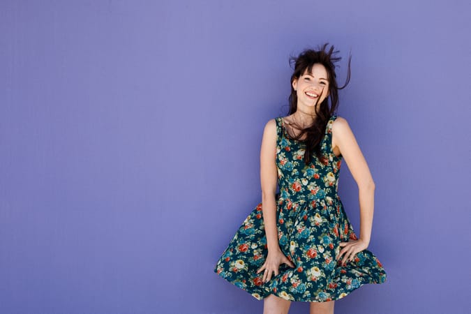 A young Thai woman in a colorful dress is smiling and posing
